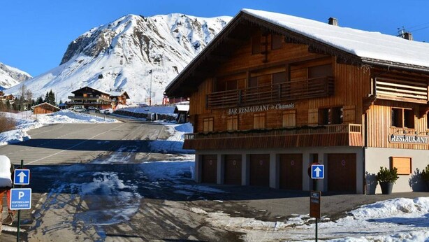 A wooden building labeled "BAR RESTAURANT Le Chamois" with a mountain backdrop. - Studio Cabin 4 Sleeps, Ski-In/Ski-Out, South-Facing Balcony, Le Grand-Bornand (Le Grand-Bornand)