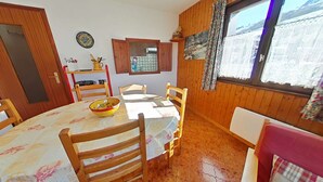 A dining area with a wooden table and chairs, a bowl on the table, and a window with curtains. - Studio Cabin 4 Sleeps, Ski-In/Ski-Out, South-Facing Balcony, Le Grand-Bornand (Le Grand-Bornand)