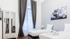 Een hotelkamer met twee bedden, een kledingkast, een groot raam met gordijnen en een schilderij aan de muur.