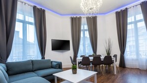 Een moderne woonkamer met een hoekbank, een eettafel met stoelen, een flatscreen televisie en een kroonluchter.