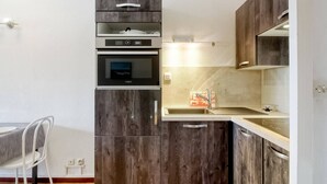 Eine kleine Küche mit dunklen Holzschränken, einem eingebauten Ofen und einer Spüle aus Edelstahl.