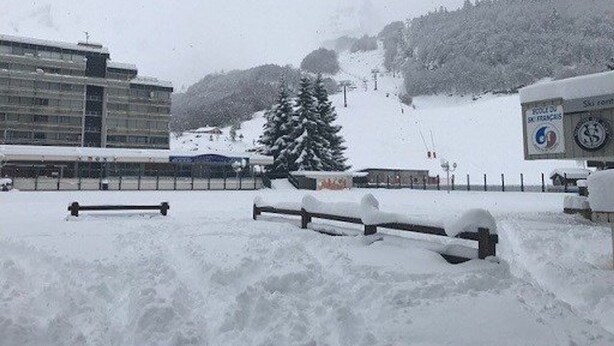 Schneebedeckte Landschaft mit Seilbahn, Gebäude und einem großen immergrünen Baum.