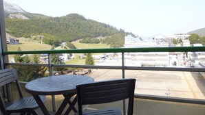 Ein Balkon mit zwei Stühlen und einem Tisch, der auf eine grüne Landschaft mit Gebäuden im Hintergrund blickt.