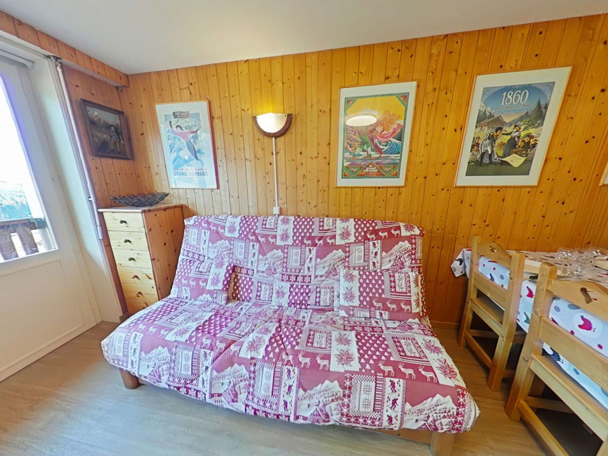Una habitación con pared de madera, cama con colcha estampada, escritorio y sillas, y una ventana.