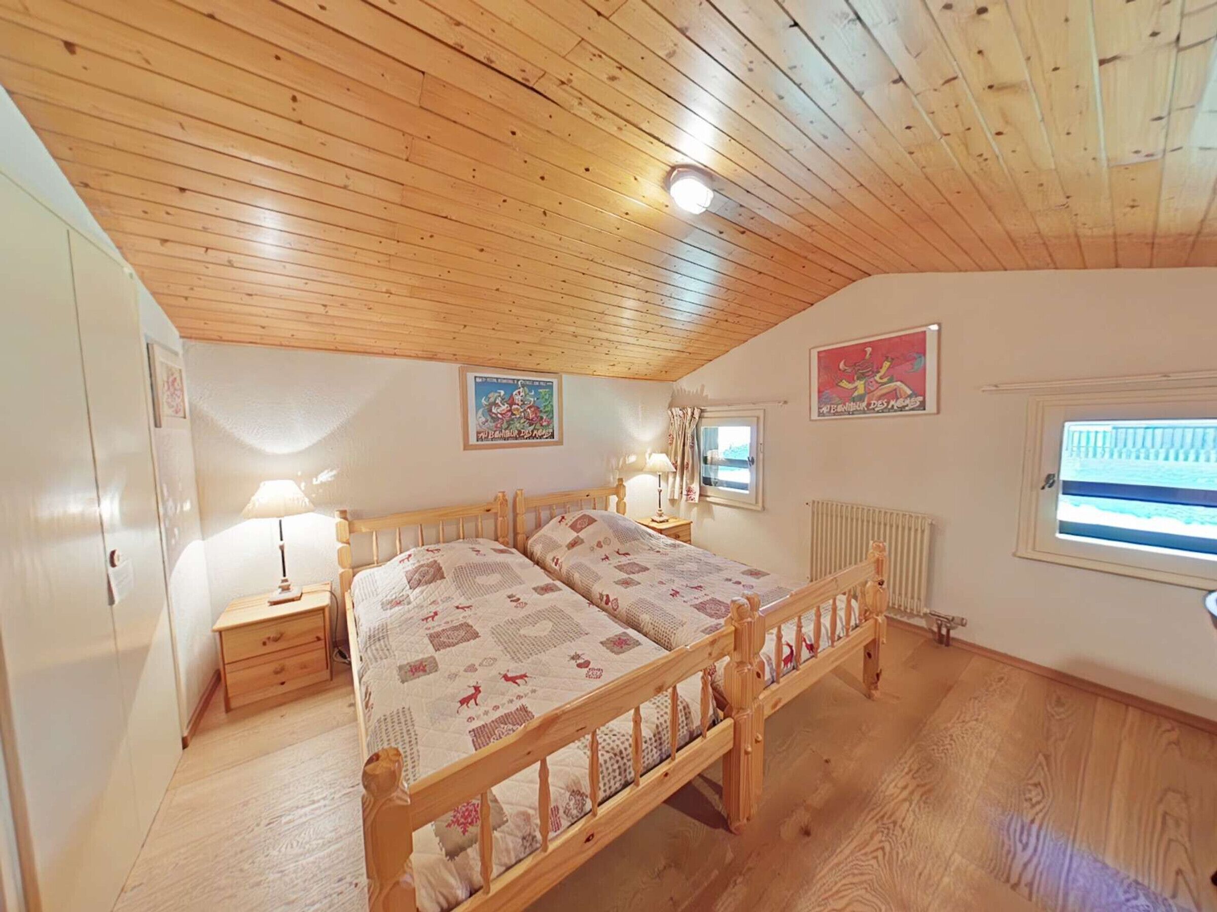 A cozy bedroom with a wooden ceiling, a double bed with patterned bedding, bedside tables with lamps, and two wall-mounted pictures.