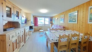 Ett rum med träpanel på väggarna, ett matbord för fyra personer, en tv och ett fönster med gardiner.