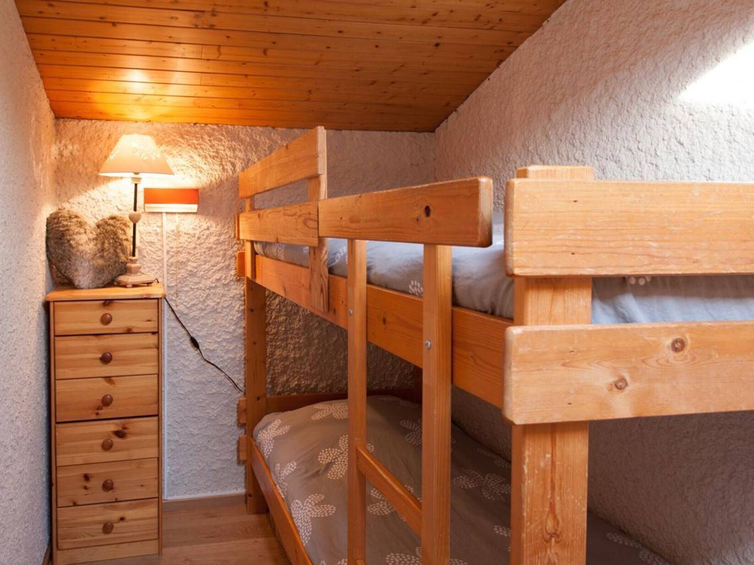 A bunk bed room with a wooden dresser and a lamp.