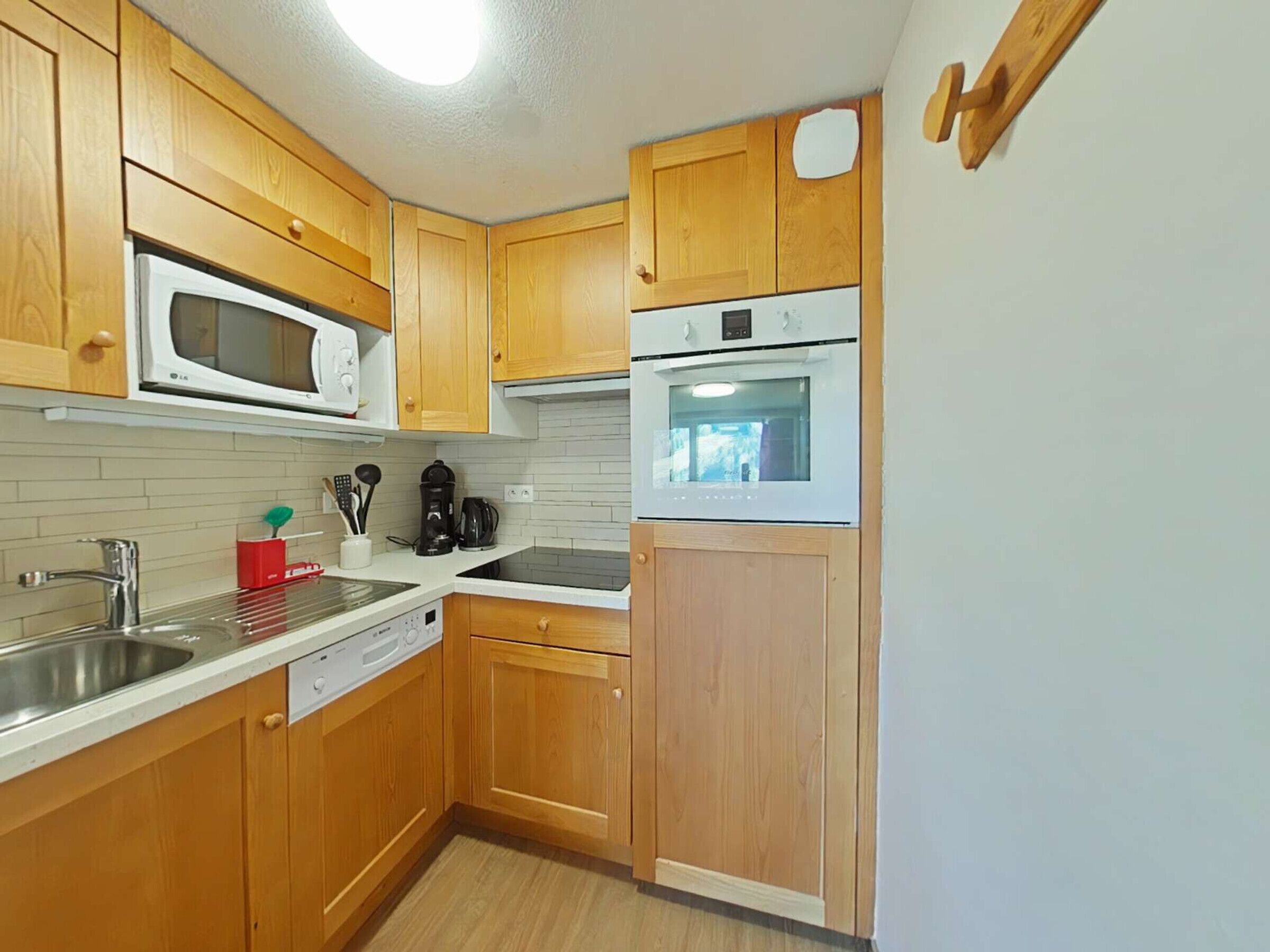 A compact kitchen with wooden cabinets, a microwave, an oven, a sink, and a coffee maker.