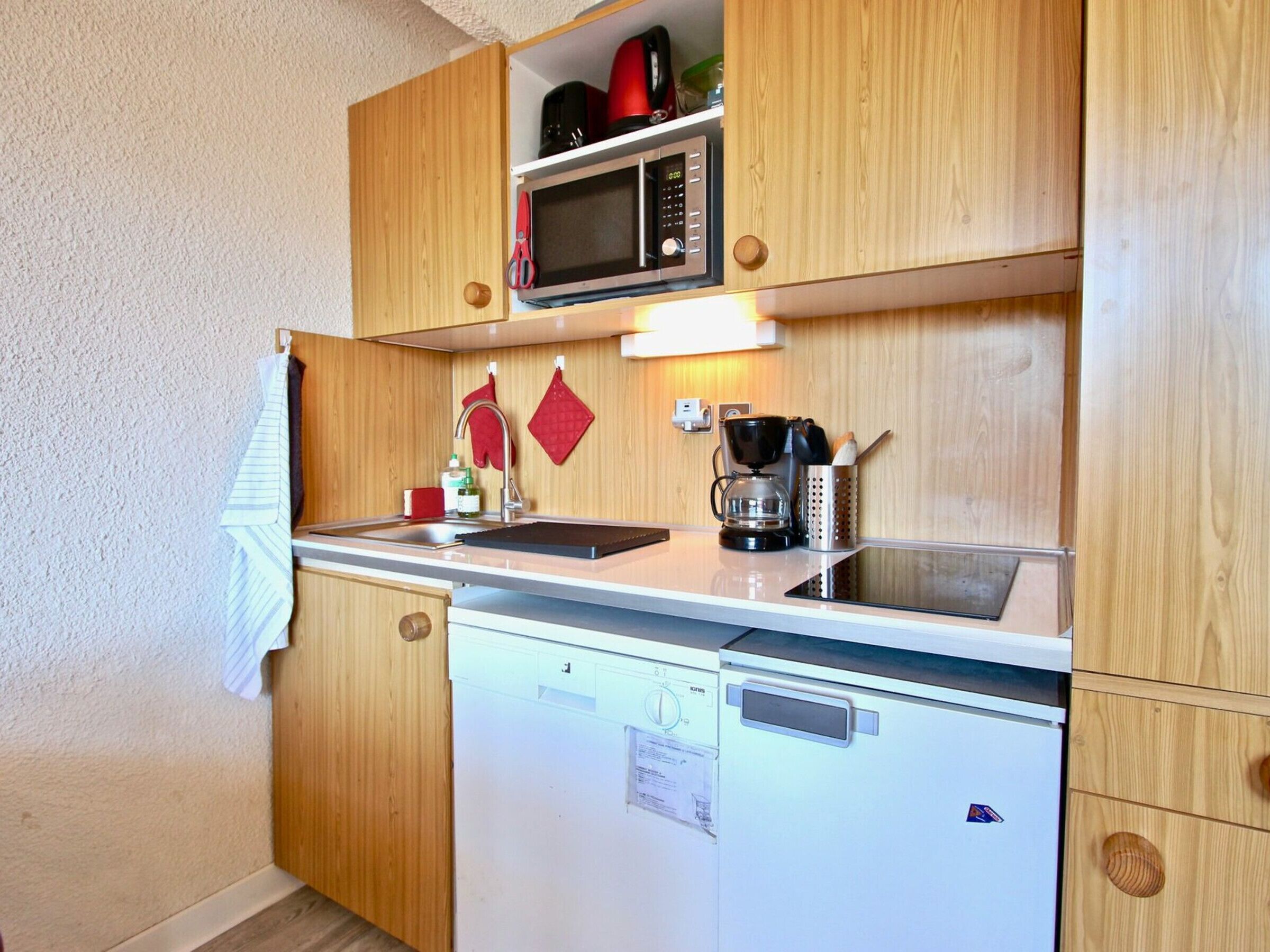 A compact kitchen with wooden cabinets, a microwave, a coffee maker, and a dishwasher.