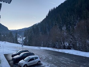 A parking area with cars, a road, and a forested mountain backdrop.