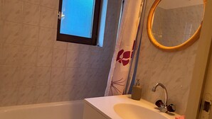 Een badkamer met een bad, een wastafel met spiegel en een raam.
