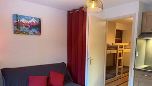 Een kamer met een bank, een rood gordijn, een schilderij en een kitchenette.