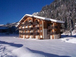 Ein mehrstöckiges Gebäude mit Balkonen, umgeben von Schnee und Bäumen.