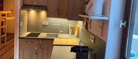 A compact kitchen with wooden cabinets, a built-in stove, a coffee machine, and a window.
