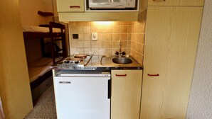 A compact kitchen with a microwave, sink, and a small refrigerator. There is a bunk bed in the adjacent room. - Studio with balcony, covered parking in Chamrousse (Chamrousse)