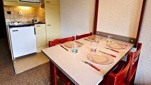 A compact kitchen with a microwave, a small refrigerator, and a dining table set for four with red chairs. - Studio with balcony, covered parking in Chamrousse (Chamrousse)