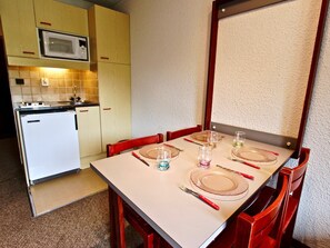 A compact kitchen with a microwave, a small refrigerator, and a dining table set for four with red chairs.