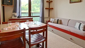 A dining area with a table set for two, a sofa, and a television on the wall. - Studio with balcony, covered parking in Chamrousse (Chamrousse)