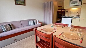 A cozy room with a sofa, a dining table set for two, and a kitchen area with a microwave. - Studio with balcony, covered parking in Chamrousse (Chamrousse)