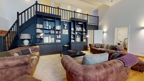A spacious living room with a dark blue staircase, leather sofas, a coffee table, and a bookshelf filled with books and decorative items. - haussmann duplex 5br 3bth city center 225m2 (Colmar)