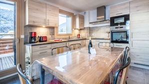 A modern kitchen with wooden cabinets, a large dining table, and built-in appliances. - Joux Plane A202 Beautiful central apartment 8 ppl (MORZINE)