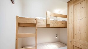 A bunk bed with a wooden frame and white bedding, a wooden wardrobe, and a wall-mounted light fixture. - Joux Plane A202 Beautiful central apartment 8 ppl (MORZINE)