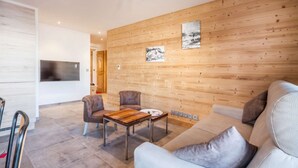 A modern living room with a wooden wall, a sofa, two armchairs, a coffee table, and a flat-screen TV. - Joux Plane A202 Beautiful central apartment 8 ppl (MORZINE)