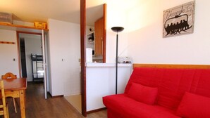 A compact living space with a red sofa, wooden dining table, and a kitchenette. - Cozy 2-Room Apartment for 6, Near Ski Lifts & Shops - L'Alpe d'Huez (Huez)