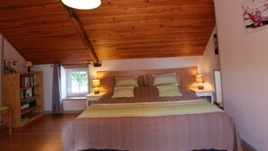 A bedroom with a wooden ceiling, a bed with multiple pillows, bedside lamps, and a bookshelf. - Cozy detached house with fireplace and enclosed garden in Normandy (Couville)