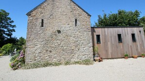 A stone building with a chimney, a wooden structure to the right, and potted plants in front. - Cozy detached house with fireplace and enclosed garden in Normandy (Couville)