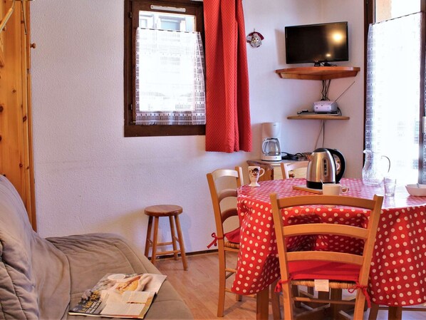 A cozy room with a wooden sofa, a dining table with chairs, a TV on a shelf, and a window with curtains. - Perfect Ski Apartment for 5 in Risoul 1850, Close to Lifts & Shops (Risoul)