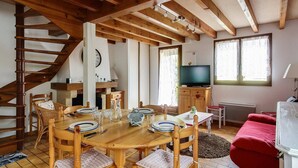 Un coin repas chaleureux avec une table et des chaises en bois, une cheminée, un téléviseur et un canapé rouge.