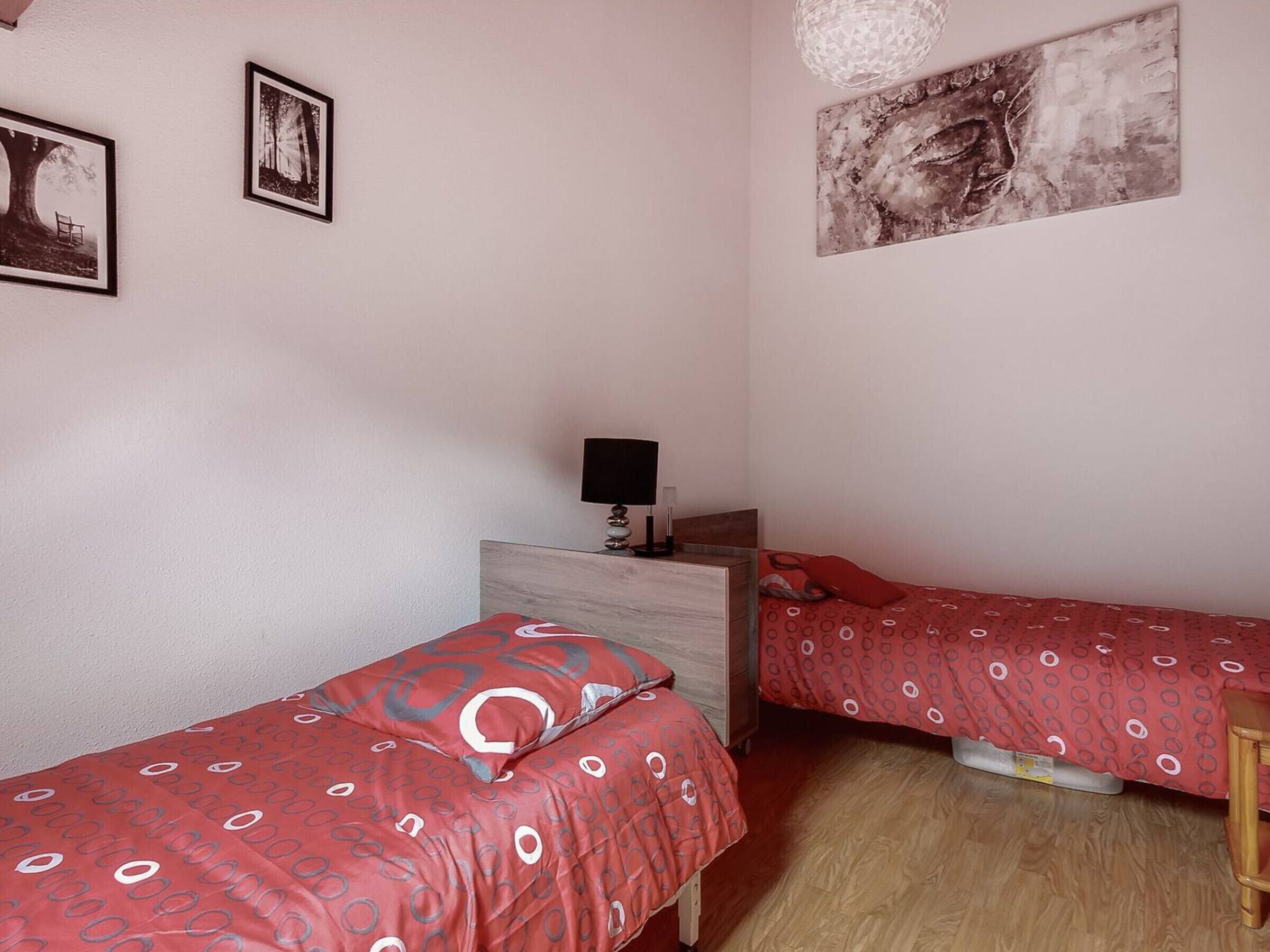 Une chambre avec deux lits simples, une table de chevet avec une lampe et une œuvre d’art accrochée au mur.
