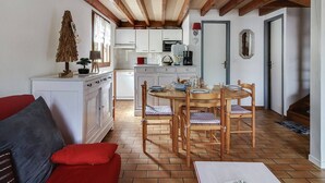 Une cuisine chaleureuse avec des poutres en bois, des meubles blancs et un coin repas comprenant une table ronde et des chaises.