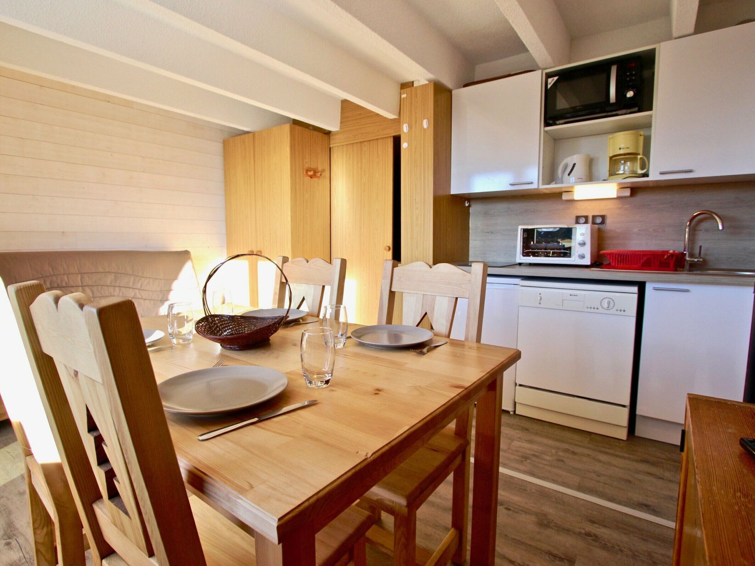 A compact kitchen with wooden cabinets, a microwave, a coffee maker, and a dishwasher.