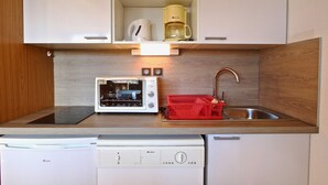 Une petite cuisine équipée comprenant un micro-ondes, un grille-pain et une machine à café sur le plan de travail, un lave-vaisselle en dessous, et un panier rouge pour les ustensiles.