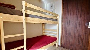 Un lit superposé avec un matelas rouge, une structure en bois et une porte marron en arrière-plan.