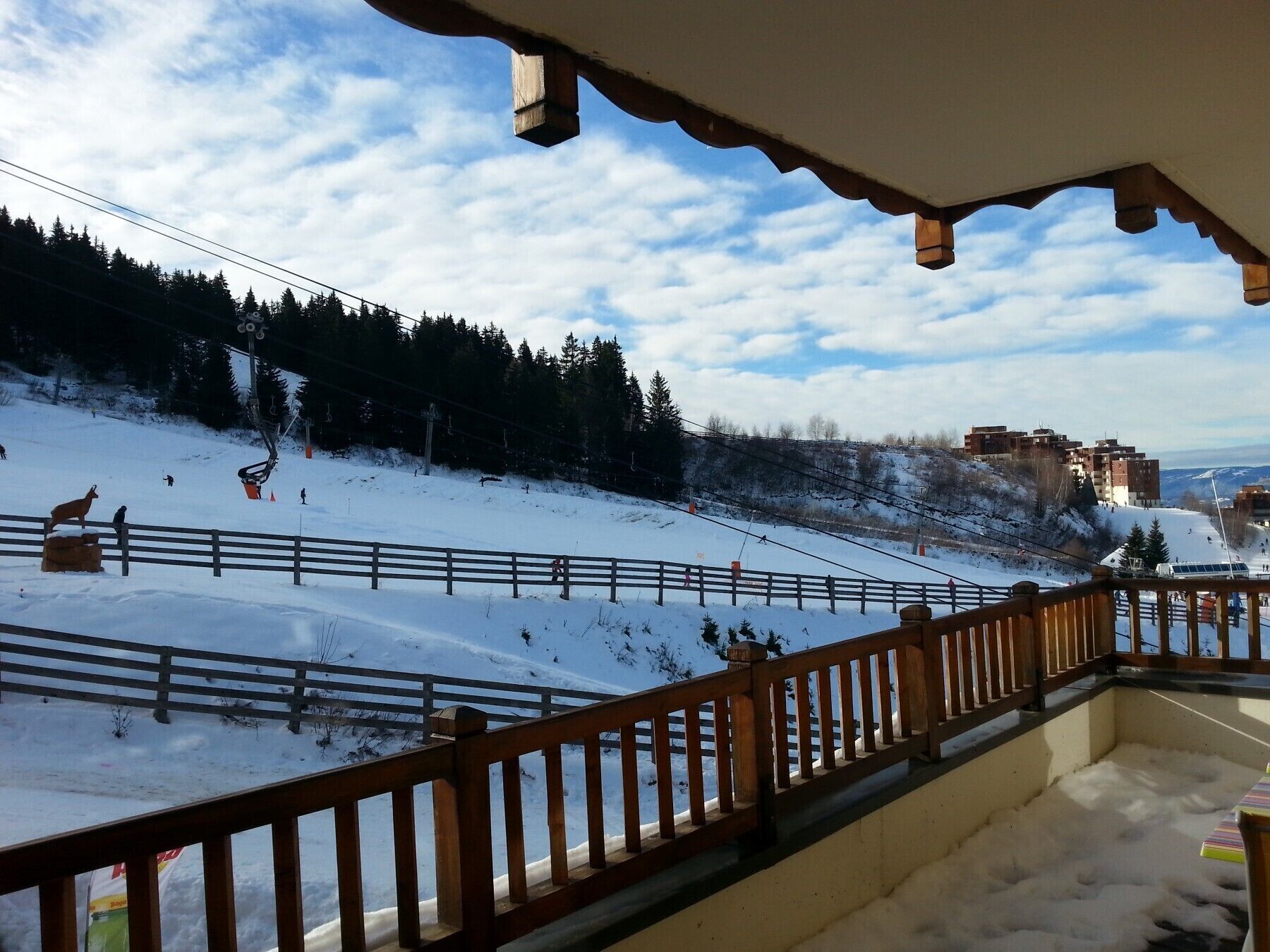 Un balcon avec vue sur une piste de ski enneigée et une ville au loin.
