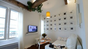 A cozy living room with a television, a white sofa, a small table with a vase and plates, and a wall decorated with framed pictures. - E5DG Discovery (París)