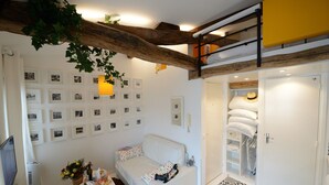 A cozy room with a white sofa, a dining table set with plates and a vase of flowers, and a wall decorated with framed photos. - E5DG Discovery (París)