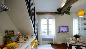 A kitchen with a white fridge, a yellow counter, and a dining area with a table and chairs. - E5DG Discovery (París)