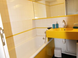 Un baño con un lavamanos amarillo, azulejos blancos y una bañera.