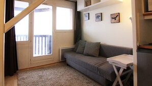 A cozy living room with a grey sofa, a small table, and a staircase leading to a balcony.