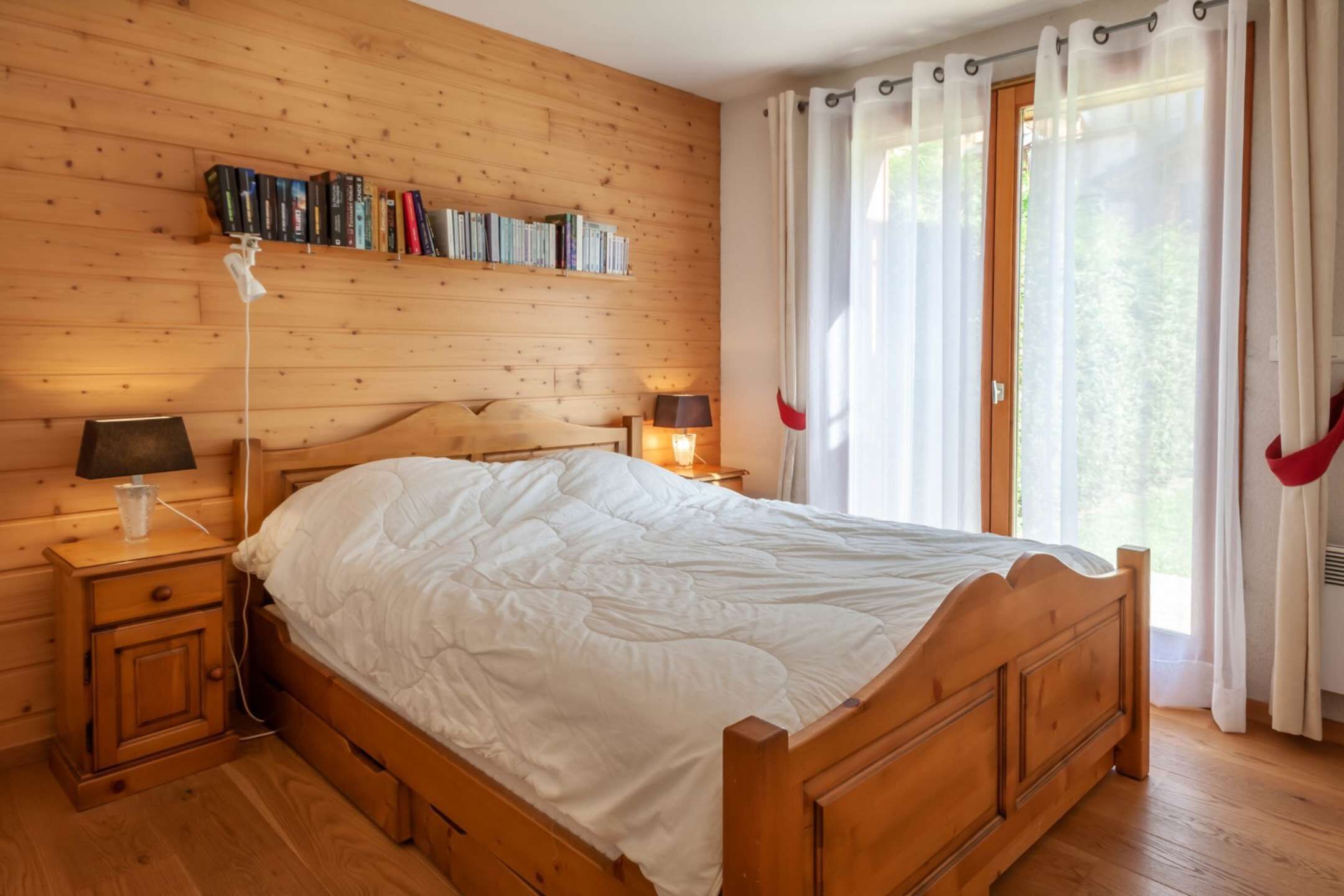 A wooden-paneled bedroom with a bed, bedside tables, a lamp, and a bookshelf.