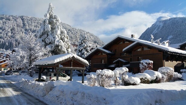 A wooden lodge with a covered patio and snow-covered surroundings. - Jeanette 2 : Nice sunny apartment with terrace (MORZINE)