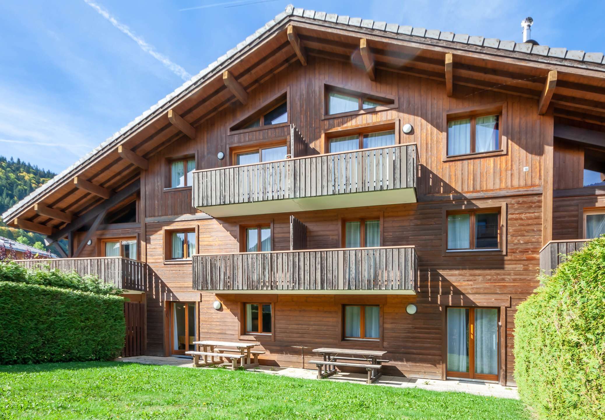 Una chaleta de madera de varios pisos con balcones, mobiliario exterior y un jardín cuidado.