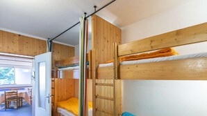 A bunk bed room with a wooden door, a small table, and a view of the outdoors.