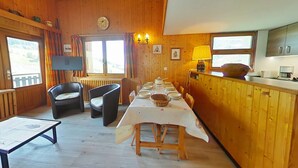 Un intérieur en bois comprenant une table à manger pour quatre personnes, un canapé, un téléviseur et un coin cuisine avec une cuisinière et des placards.