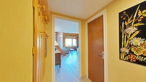 Un couloir aux murs jaunes, une porte en bois et un tableau représentant des fleurs.