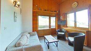 Une pièce chaleureuse avec un plafond en bois, un canapé, un fauteuil, une petite table et un téléviseur.